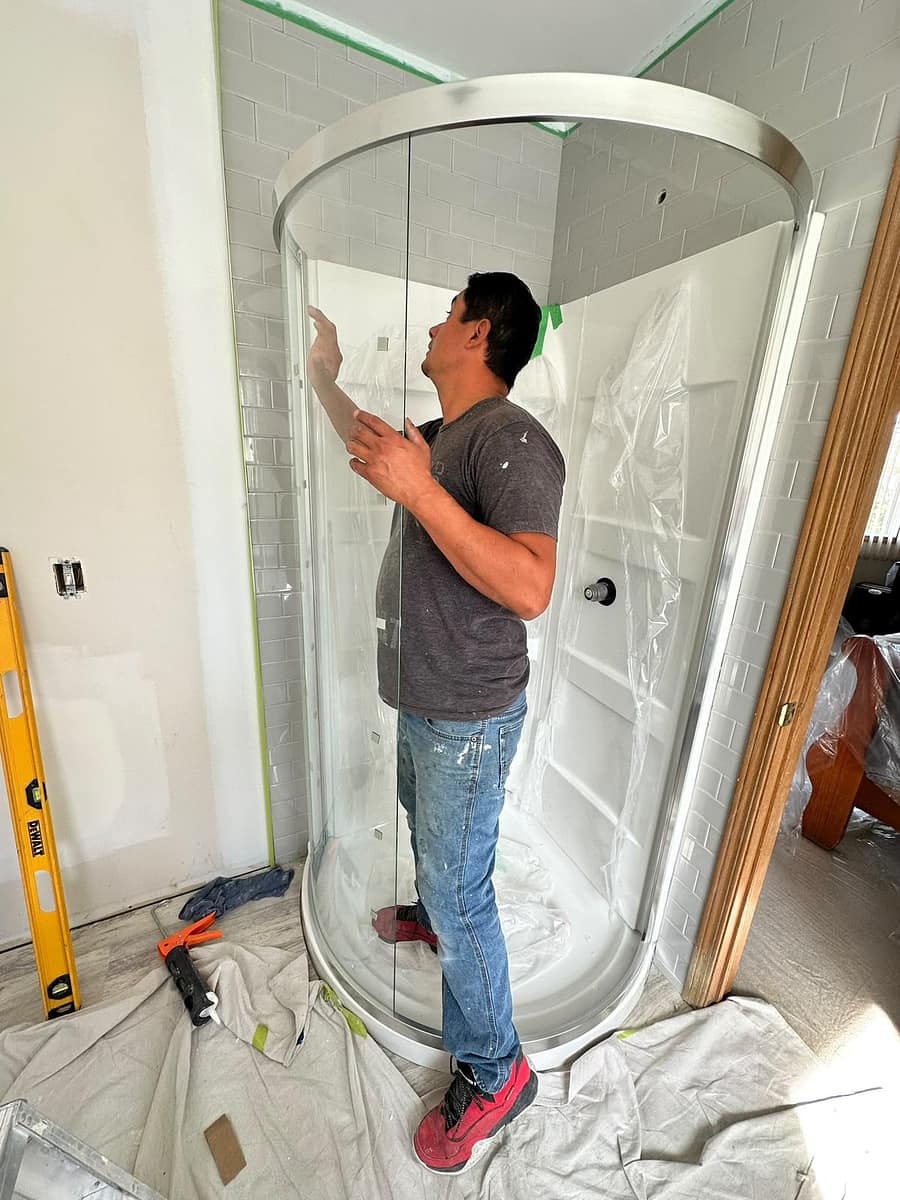Bathroom Renovation (Tamarack) — installer fitting the curved glass shower enclosure against subway-tiled walls