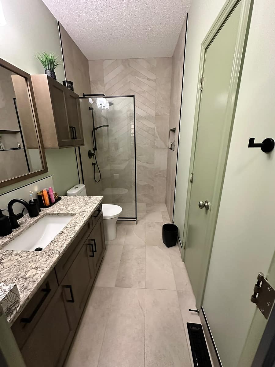 Bungalow Home Renovation — completed bathroom viewed from the entrance, showing sage green walls, brown vanity, walk-in shower with black-framed glass and herringbone feature wall