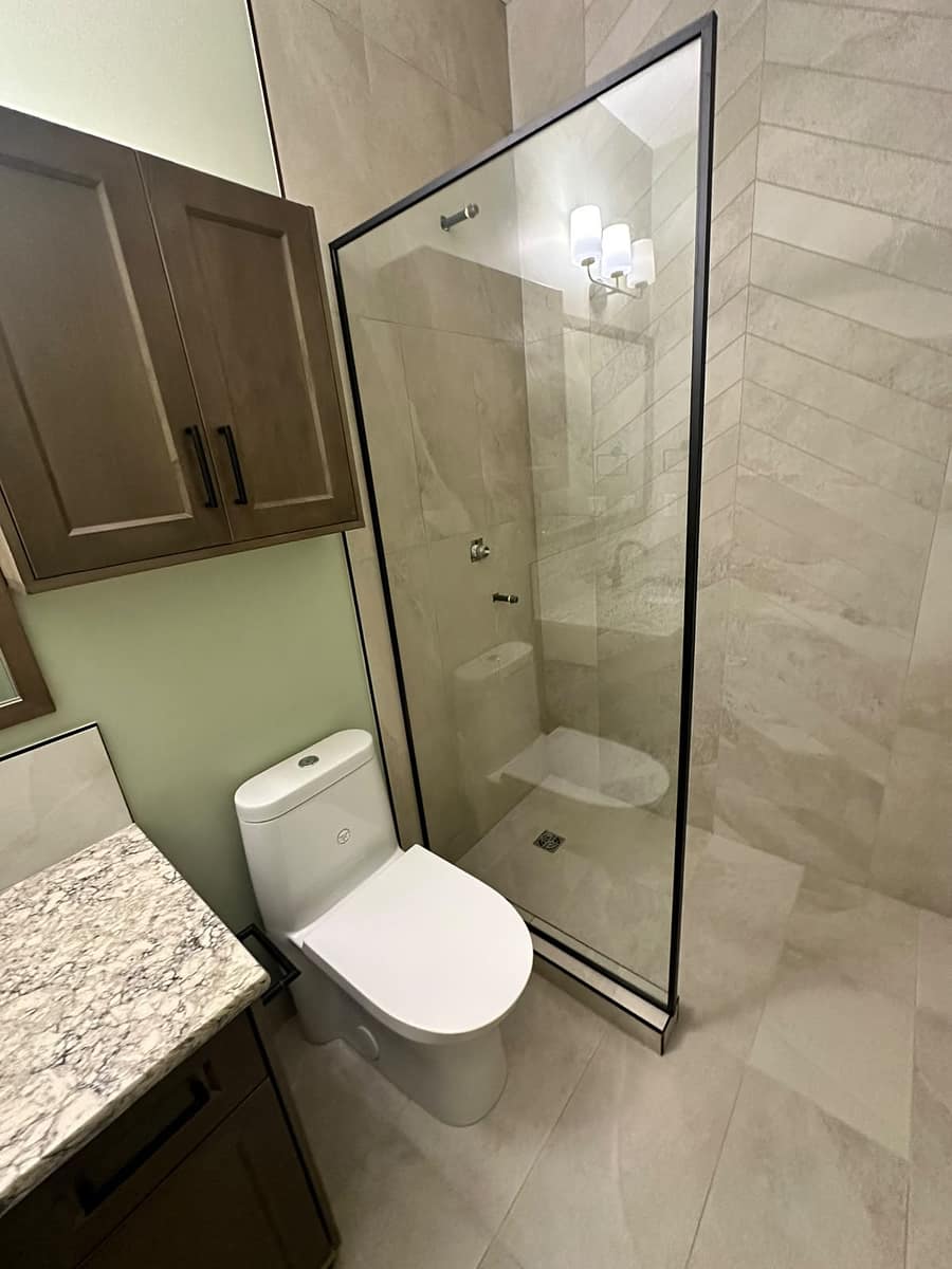 Bungalow Home Renovation — high-angle view of the toilet and walk-in shower entrance with black-framed glass partition and large-format beige tile