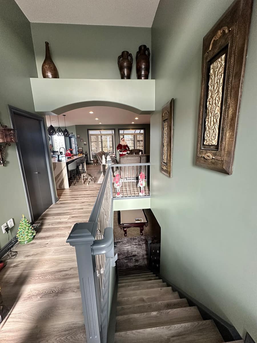 Bungalow Home Renovation — upper-level hallway with light wood flooring, sage green walls and arched doorway to the living area