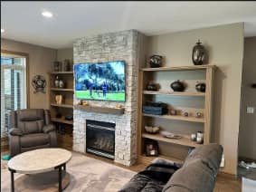 Bungalow Home Renovation — living room with stacked-stone fireplace, mounted TV, wood mantel and built-in shelving