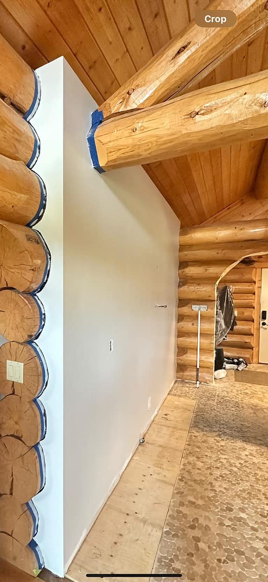 Custom Log Home Interior Renovation — finished drywall partition meeting the original log wall, sealed seam with painter's tape, wood-plank ceiling and pebble-tile floor