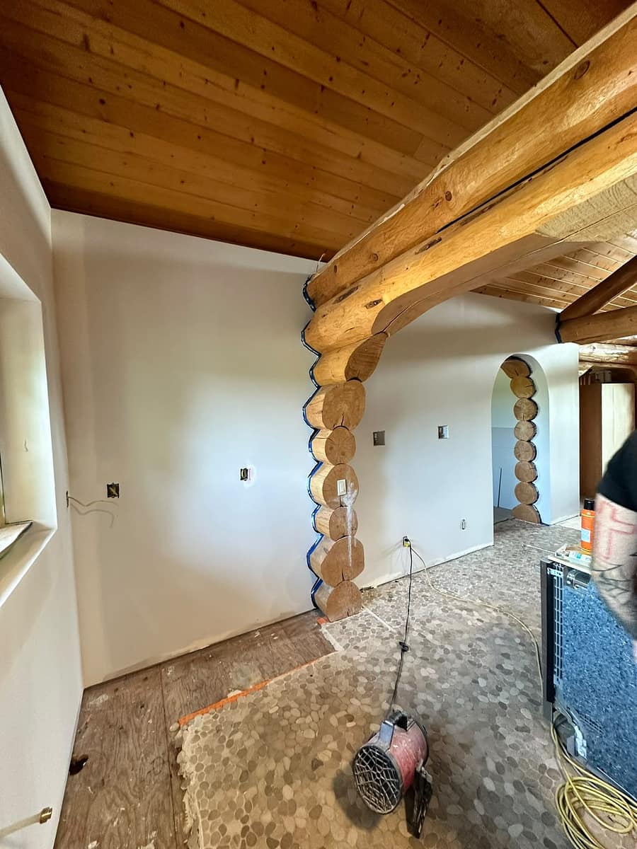 Custom Log Home Interior Renovation — wide view of the white drywall partition with two arched openings integrating with the log beams and timber ceiling