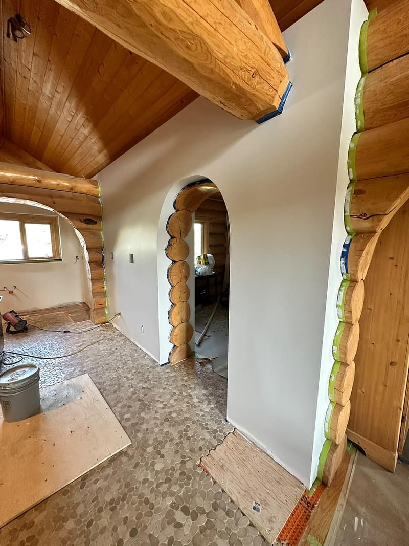 Custom Log Home Interior Renovation — alternate angle showing the white walls wrapping around the round log structure, seams taped and sealed