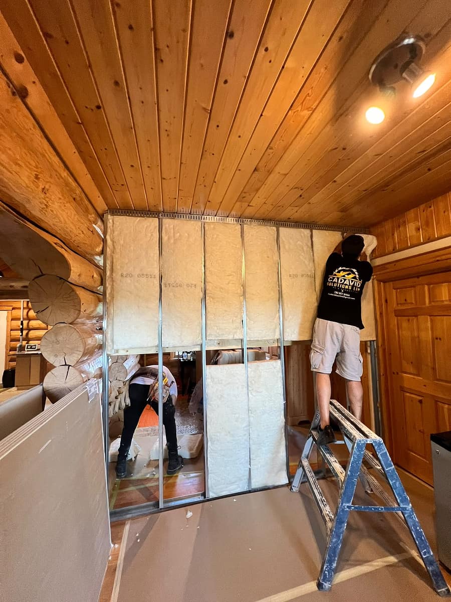 Custom Log Home Interior Renovation — R-20 insulation batts and plywood backing installed within the custom metal framing around the original logs