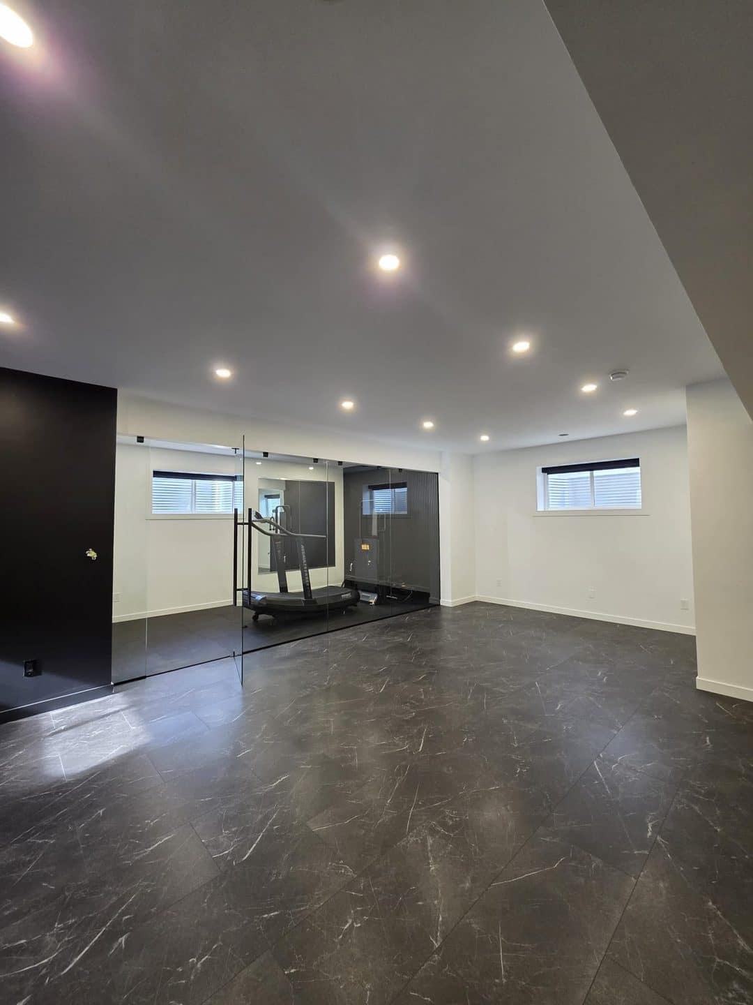 Basement Development — spacious basement room with dark marble tile flooring and a glass-enclosed curved treadmill gym area