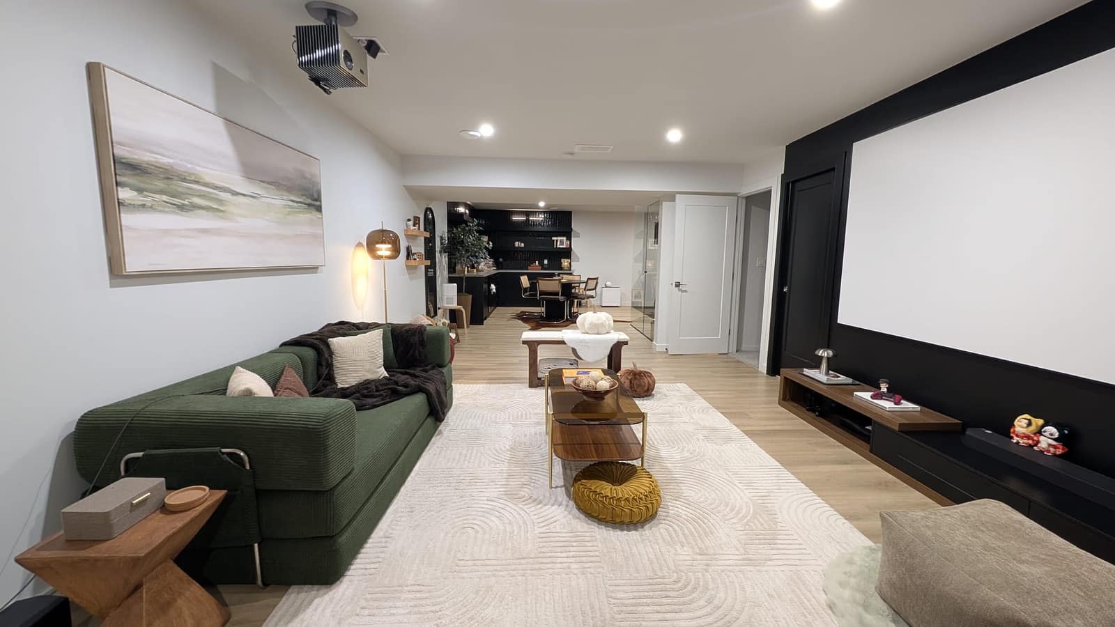 South Edmonton basement living room with green sofa, projector screen and open view to the kitchen and dining area