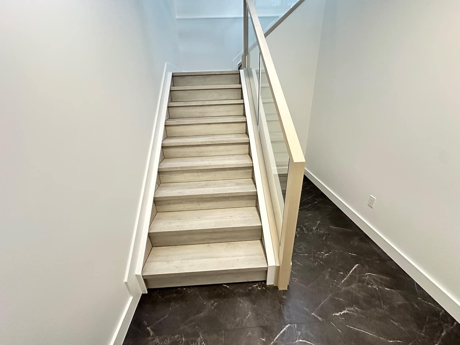 Basement staircase after finishing — premium treads, glass railing and dark flooring