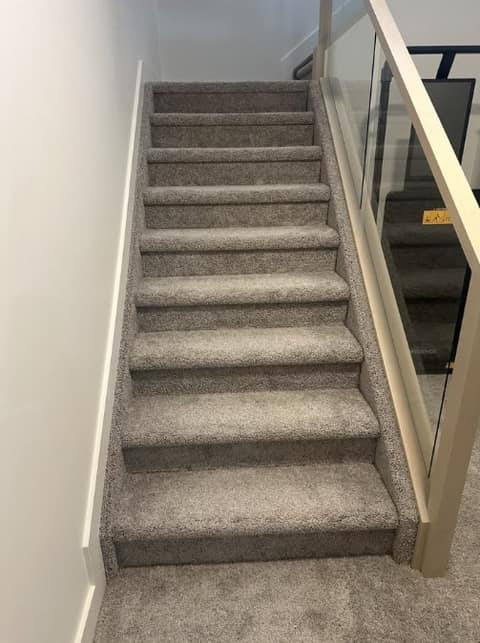 Basement staircase before finishing — carpeted stairs and plain railing